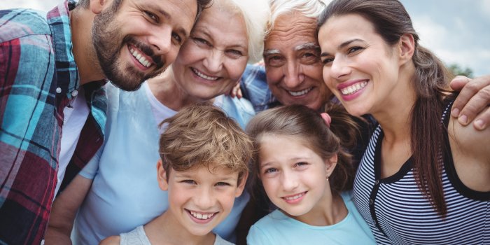Ein Gruppenbild einer Familie, die lächelnd in die Kamera schaut. Von Großeltern über Eltern und Kinder ist alles vertreten.