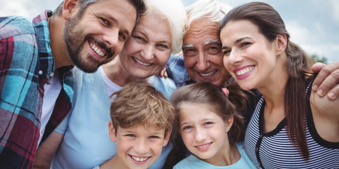 Ein Gruppenbild einer Familie, die lächelnd in die Kamera schaut. Von Großeltern über Eltern und Kinder ist alles vertreten.