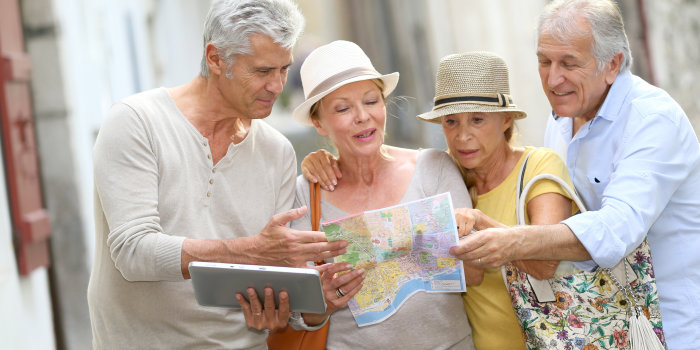 Vier alte Freunde sind auf einem Städtetrip und beraten sich gerade mit Stadtkarte und elektronischen Navigationsgerät, welchen Weg sie nehmen sollen.