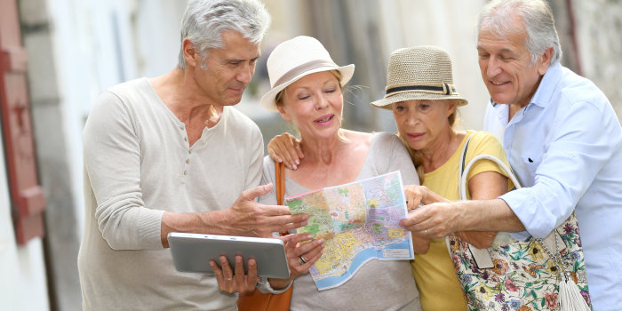 Grafik: Reisen mit Freunden © goodluz/Fotolia Vier alte Freunde sind auf einem Städtetrip und beraten sich gerade mit Stadtkarte und elektronischen Navigationsgerät, welchen Weg sie nehmen sollen.
