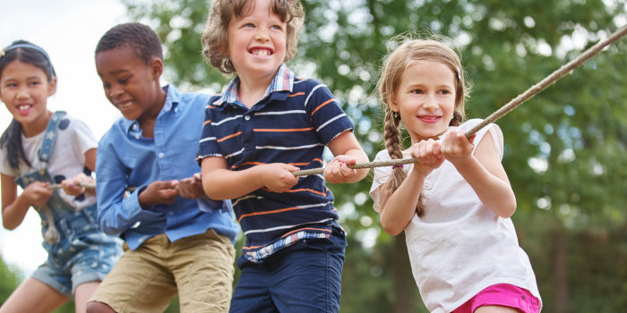 Vier Kinder ziehen, offensichtlich während eines Wettkampfes, draußen im Grünen gemeinsam an einem Seil.