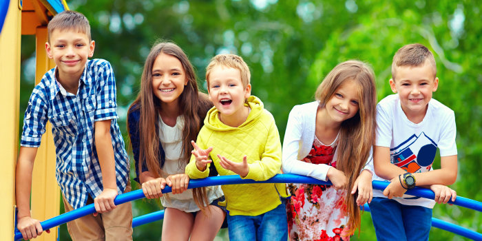 Fünf Kinder stehen auf einem Klettergerüst im Grünen und lächeln in die Kamera.