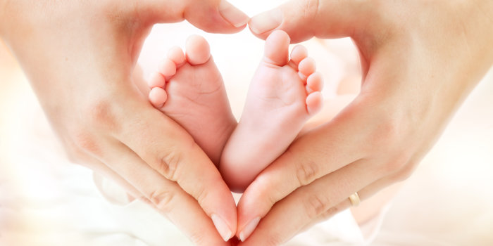 Zwei zu einem Herz geformte Hände einer Frau umrahmen zwei kleine Füße eines Babys.