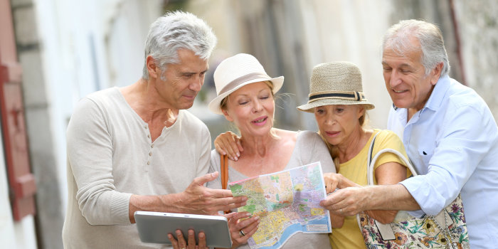 Vier alte Freunde sind auf einem Städtetrip und beraten sich gerade mit Stadtkarte und elektronischen Navigationsgerät, welchen Weg sie nehmen sollen.