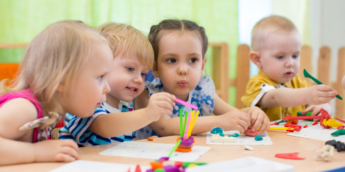 Vier Kleinkinder spielen in der Kindertagesstätte mit Knetmasse.