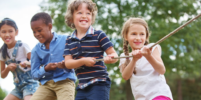 Vier Kinder ziehen, offensichtlich während eines Wettkampfes, draußen im Grünen gemeinsam an einem Seil.