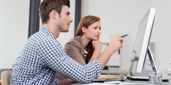 Foto: Arbeiten am PC © contrastwerkstatt/Fotolia Ein mittdreißiger Mitarbeiter zeigt seiner gleichaltrigen Kollegin an einem Computerbildschirm Sachen auf. Ein Ordner mit Unterlagen liegt vor ihnen.