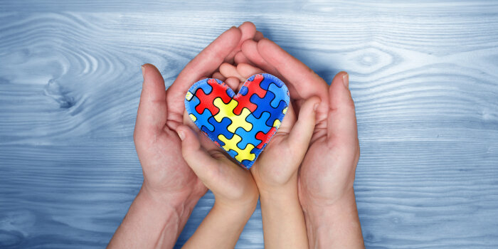 Hände von Kind und Erwachsenem halten ein buntes Puzzleherz