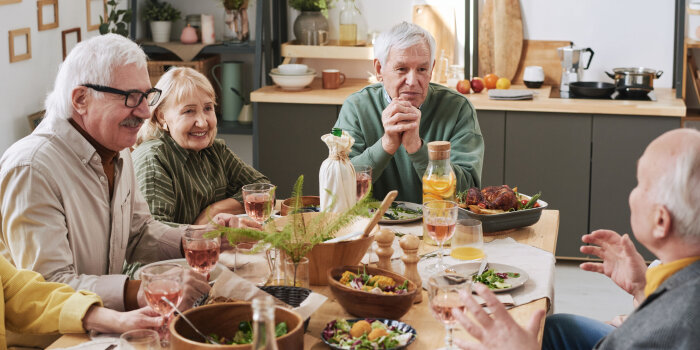 Senioren sitzen um einen Tisch mit Salat und Essen.