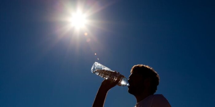 Ein Mann trinkt im Gegenlicht Wasser aus einer Plastikflasche. 