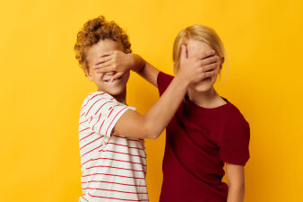 Foto: Kinder halten sich die Augen zu © Stadtverwaltung Erfurt/kulyashina/123rf Zwei Kinder, vor einem gelben Hintergrund, halten sich gegenseitig die Augen zu.