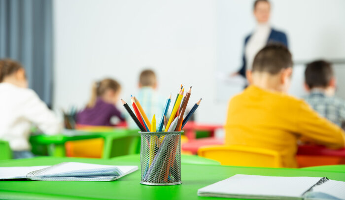 Ein Stifthalter mit Stiften steht in einem Klassenraum.