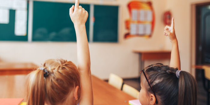 Foto: Zwei Mädchen melden sich © Stadtverwaltung Erfurt/nestea06/123rf Zwei Mädchen melden sich in einem Klassenraum. Sie sind von hinten zu sehen.