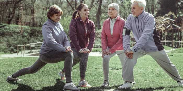 Eine Gruppe aus zwei älteren Frauen, einer jungen Frau und eines älteren Mannes dehnen sich vor dem Sport.