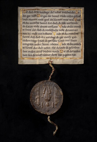 Schriftstück mit alter Schrift in Gold und Schwarz an dem ein Siegel 