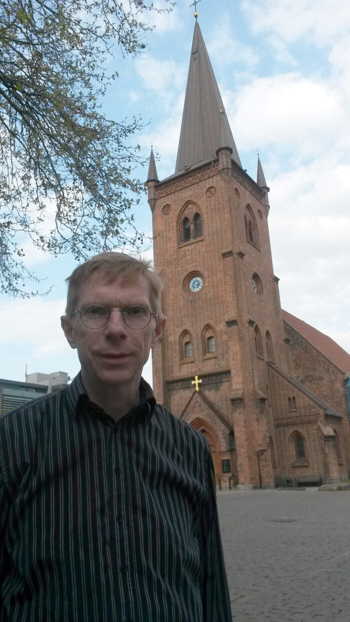 Erik Kure Mann mit Brille und schwarzen Hemd, vor einer kleinen Kirche