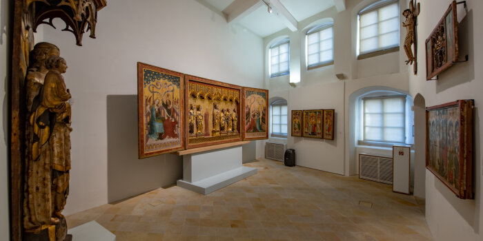 Raumaufnahme im Angermuseum, hoher weißer Raum mit Holztafel und Skulpturen an den Wänden 