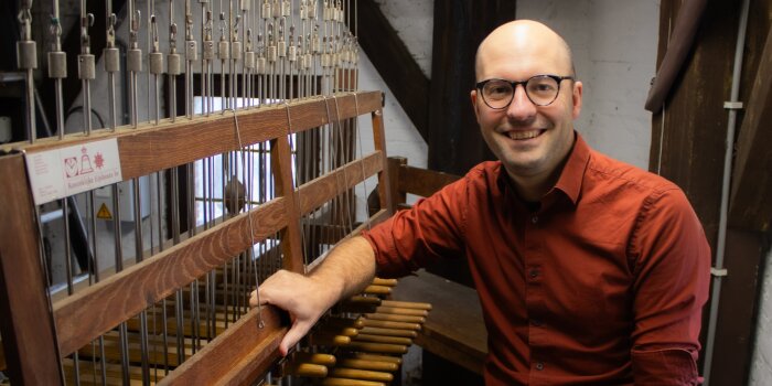 Mann mitteleren Alters in einem roten Hemd, mit Brille und wenig Haaren an einem Carillon-Spieltisch sitzend