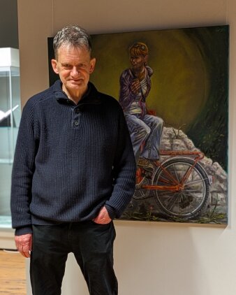 Foto: Horst Wagner in der Ausstellung © Stadtverwaltung Erfurt Mann mittleren Alters in einem dunkelblauen Wollpullover vor einem Kunstwerk mit einem Fahrrad stehend
