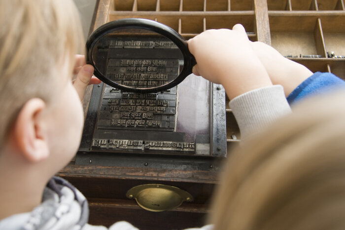 Benary-Speicher: Lettern-Setzkasten im Druckereimuseum Kinder stehen an einer Druckerpresse und drucken eine Buchseite