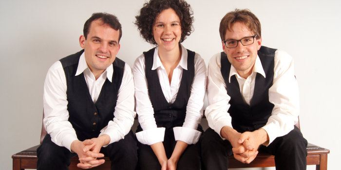 Foto: Klezmer-Trio „Rozhinkes“ © Rozhinkes zwei Männer mit Frau in der Mitte auf einer Bank sitzend