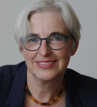 Foto: Katrin Kogman-Appel © K. Kogman-Appel Eine Frau mit kurzen grauen Haaren und schwarz umrandeter Brille lächelt in die Kamera. Sie trägt eine Kette aus verschiedenfarbigen Bernsteinperlen und ein dunkelblaues Jackett.