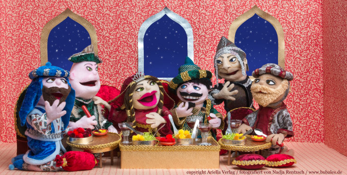 Bubales Puppentheater Sechs Stoffpuppen sitzen fröhlich um einen gedeckten Tisch herum.