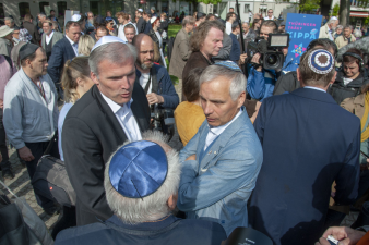 drei Männer mit kleiner Mütze im Gespräch, außenherum viele Menschen, im Hintergrund ein Kamerateam