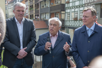 drei Männer, der mittlere hält ein Mikrofon in der Hand und spricht, im Hintergrund Krämerbrücke