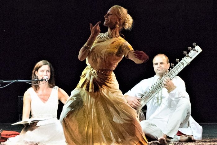 Atmadhvani – spirituelle Musik und Tanz aus Indien tanzende Frau im goldenen Kleid, dahinter zwei Musiker/innen mit Zupfinstrument und Mikrofon