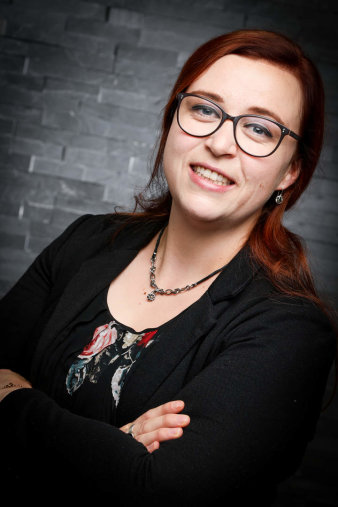 Foto: Portraitfoto Malin Drees © Malin Drees ein Foto einer Frau mit Brille, welche mit verschränkten Armen vor einer Wand steht