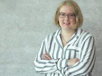 Eine Frau mit kurzen blonden Haaren und Brille in einer gestreiften Bluse blickt in die Kamera.