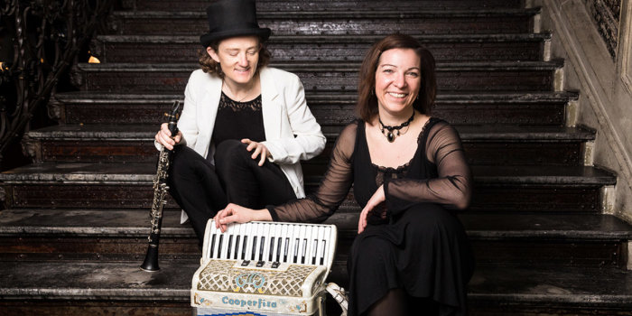 Zwei Frauen sitzen auf einer Treppe. Eine hat eine Klarinette, die zweite ein Akkordeon in  der Hand