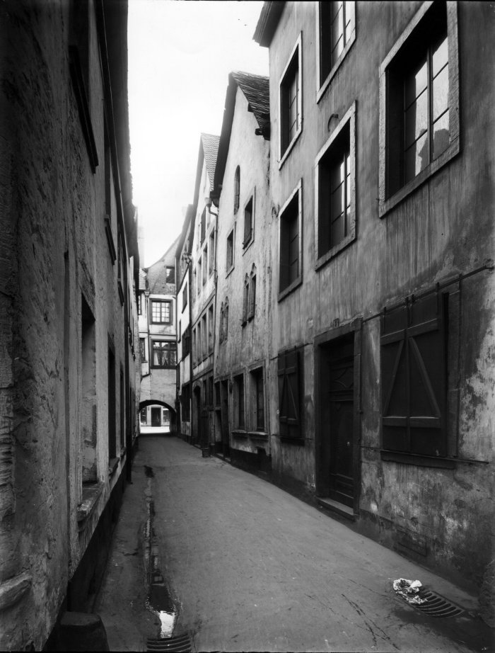 Judengasse in Trier Das Schwarz-Weiß-Foto zeigt eine enge Gasse mit drei- und vierstöckigen Häusern, am Ende befindet sich ein Torbogen
