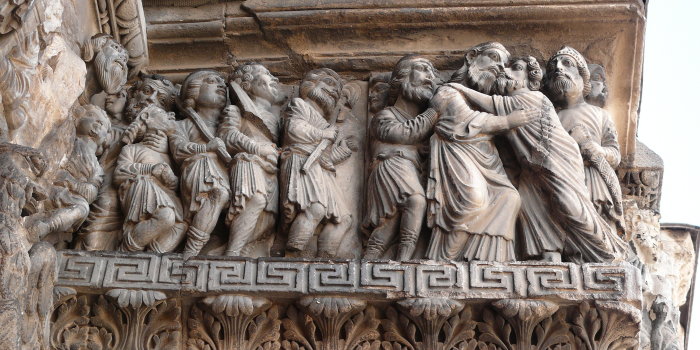 Die Aufnahme zeigt ein Relief an einer Kirche. Judas  küsst Jesus auf die Wange, andere Jünger stehen daneben. 