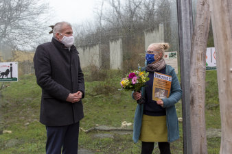 eine Frau und ein Mann stehen nebeneinander, sie tragen Mundschutz, die Frag hält Blumenstrauß und Urkunde