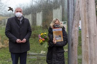 eine Frau und ein Mann stehen nebeneinander, sie tragen Mundschutz, die Frag hält Blumenstrauß und Urkunde