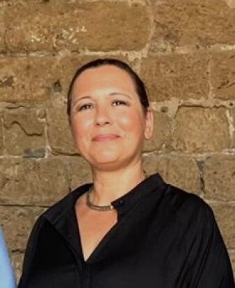 Foto: Portrait Merav Schnitzer © Stadtverwaltung Erfurt - Merav Schnitzer Schwarzhaarige Frau mittleren Alters vor Steinwand