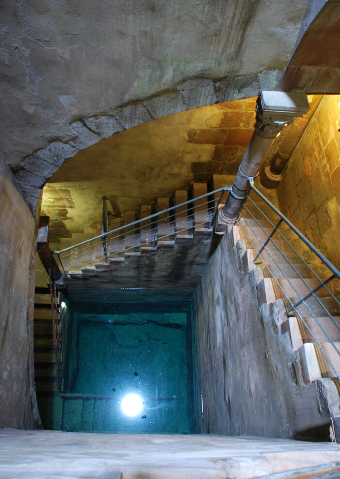 Mikwe Friedberg Ein dunkler Raum mit einer abfallenden Treppe und einem Lichtpunkt im Wasser in der Tiefe
