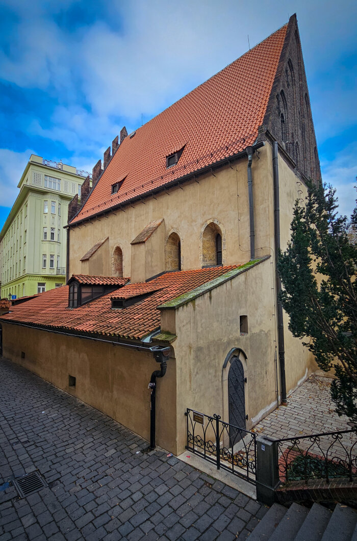 Altneuschul in Prag Eine Seitenansicht von einem Gebäude mit rotem Dach vor blauen Himmel