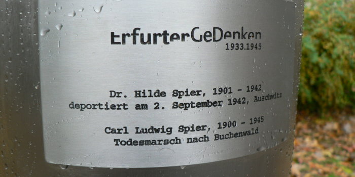 Foto: DenkNadel © Stadtverwaltung Erfurt Nahaufnahme einer Installation im Straßenraum, die wie eine große Nadel aussieht. Unter dem Nadelkopf befindet sich eine Gedenkplatte mit den biografischen Angaben einer von den Nationalsozialisten deportierten Person.