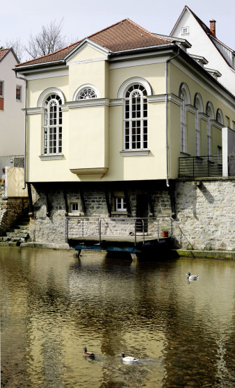 Fassade der Kleinen Synagoge zum Fluß hin. Klassizisitsches gelbes Gebäude mit großen, schmalen Fenster mit Rundbogen.