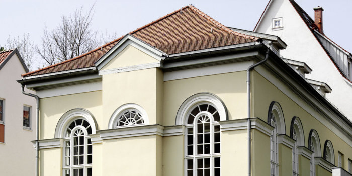 Fassade der Kleinen Synagoge zum Fluß hin. Klassizisitsches gelbes Gebäude mit großen, schmalen Fenster mit Rundbogen.