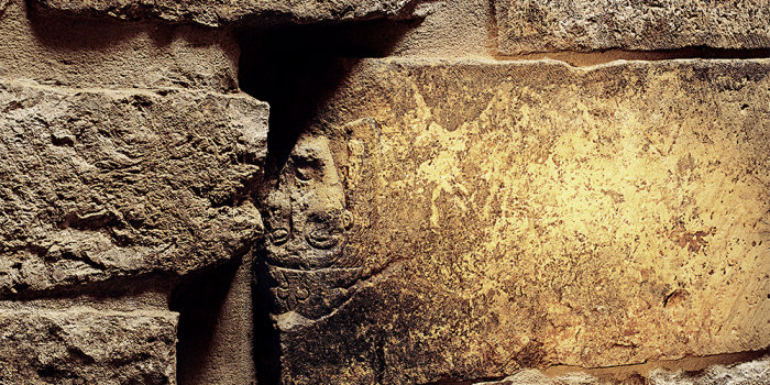 Angeleuchteter Ausschnitt der Mauer der mittelalterlichen Mikwe, der eine auf dem Kopf stehend eingemauerte Plastik aus dem 12. Jahrhundert zeigt