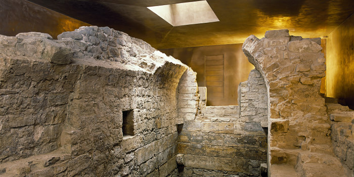 Foto: Mikwe Erfurt © Peter Seidel Mauerreste der mittelalterlichen, jüdischen Mikwe. Reste eines kleinen Raumes mit Tonnengewölbe, umgeben von Ausschnitten des bronzefarbenen Schutzbaus.
