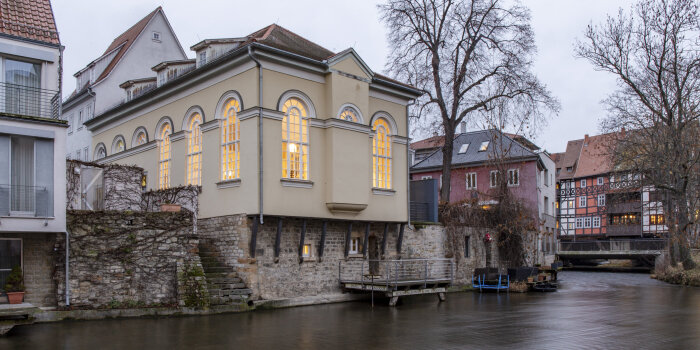 Lichter gegen Dunkelheit - Kleine Synagoge ein Haus mit großen beleuchteten Fenstern an einem Flussufer