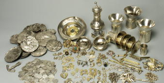 Der gesame Schatzfund ausgebreitet und sortiert in seine einzelnen Bestandteile. Münzen, Silberbecher, Silberbarren, Schmuck in diversen Arten.