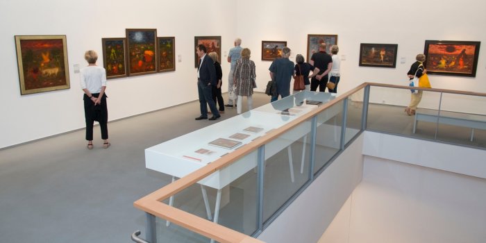 Foto: Blick in die Ausstellung „Arik Brauer. Phantastisch-realistisch. Ein Lebenswerk“ © Falko Behr Blick in die Kunsthalle, in der Besucher Bilder betrachten