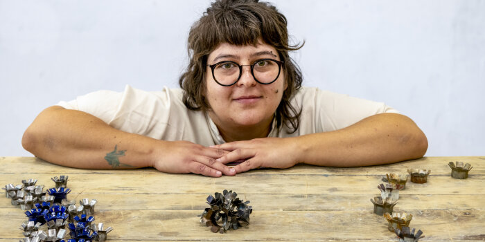 Junge Frau die hinter einem Tisch hockt, auf dem blumenartige Metallteile liegen