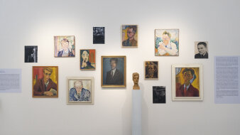 Eine weiße Wand mit vielen gemalten Portraits und einer Skulptur in der Mitte